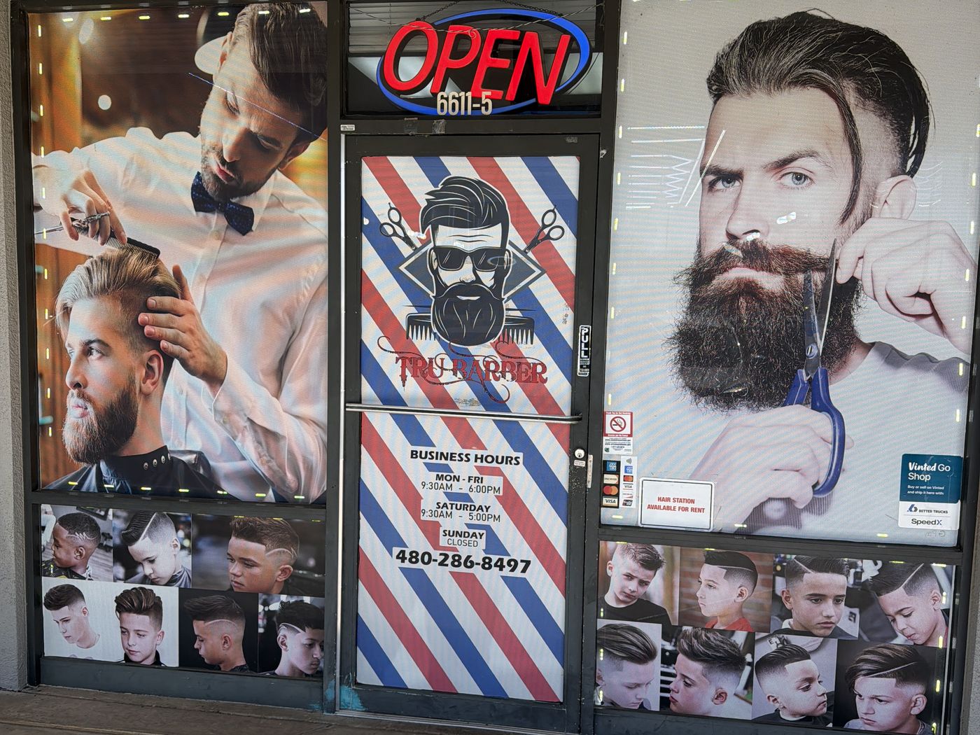 The Tru Barbershop storefront: the OPEN sign, the barber-pole striped door with the hours, and the poster windows